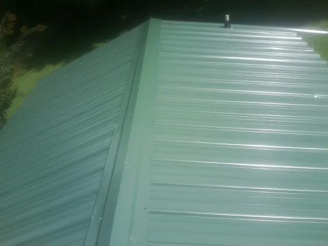 New green metal panels meeting at the ridge of a roof — Flat Roof Repair work by our crew in Thomasville