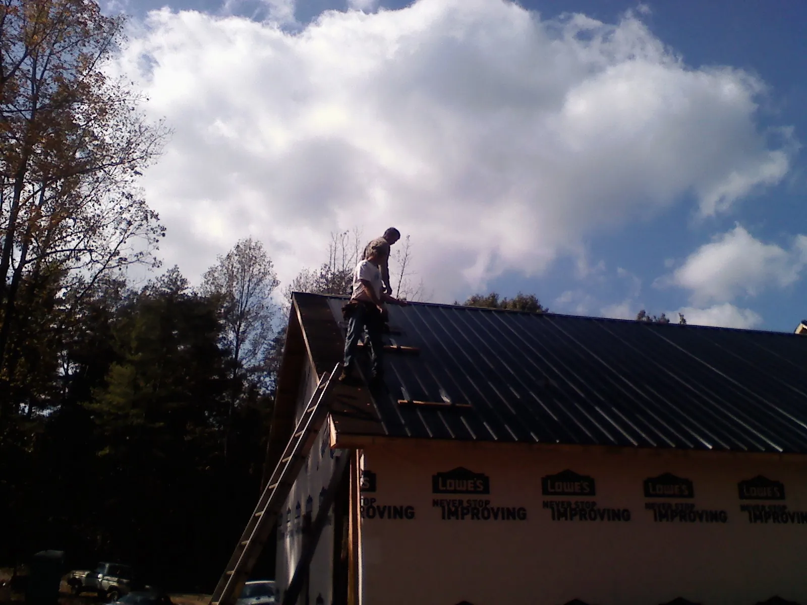 Roofer fastening dark metal panels high against a cloudy sky, from a Roof Inspection job in Thomasville